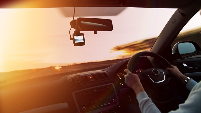 Dash cam below the rear vision mirror on a car window at sunset